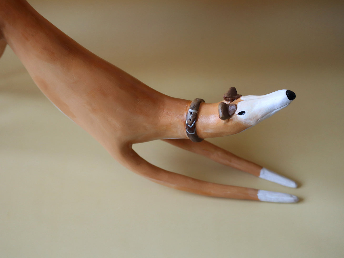 Greyhound figurine with a collar on a beige background